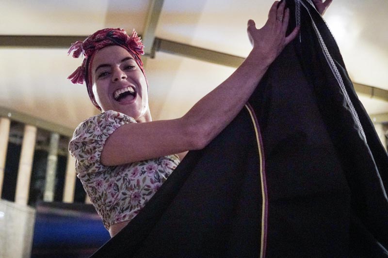 Mujer joven danza feliz. Tiene pañoleta roja en la cabeza y en sus manos entrelaza la punta la falda