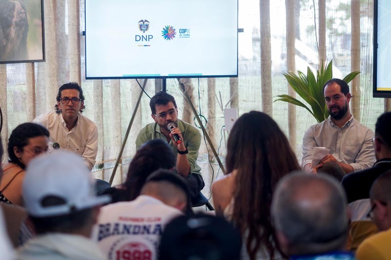 Hombre conferencista, exponiendo ante el público temas ambientales acompañado de tres panelistas.