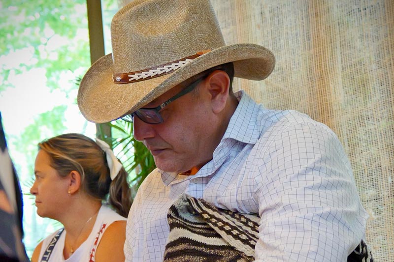 Hombre mayor con sombrero vueltiao y mochila de rayas café oscuro, toma apuntes en una libreta. 