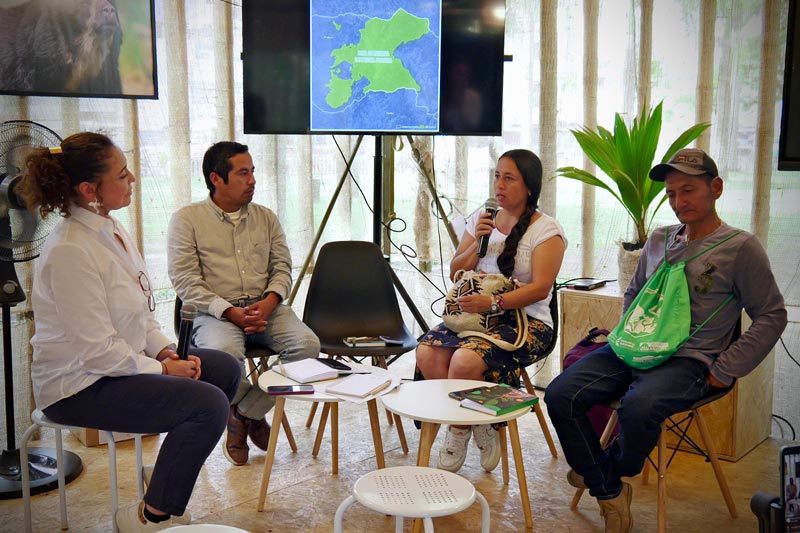 Cuatro personas sentadas en el panel principal socializan entre si los alcances de la charla en implementación social