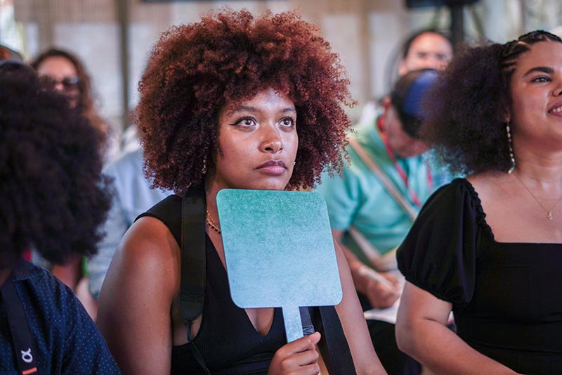 Mujer afro, tiene en la mano derecha una paleta azul que al levantarla pide participación. 