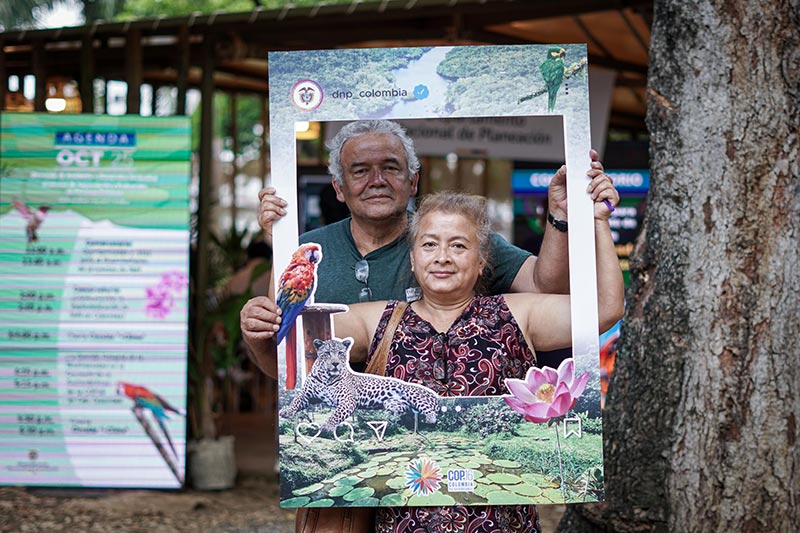 Dos adultos mayores (hombre y mujer), en foto de primer plano con el marco de la COP16.