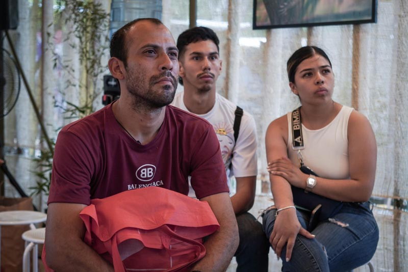 Tres personas jóvenes sentadas, observando atentamente una presentación sobre temas ambientales en un evento, con expresiones serias