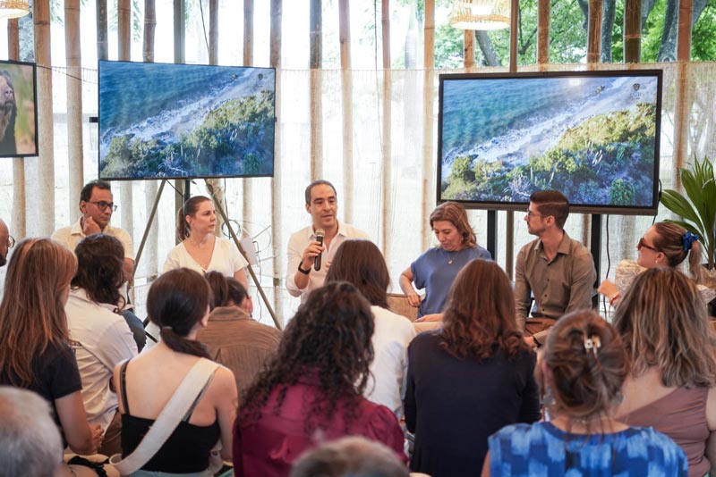 Sentados en el panel principal, dos hombres y dos mujeres, frente a ellos un grupo de personas que los escuchan atentamente.