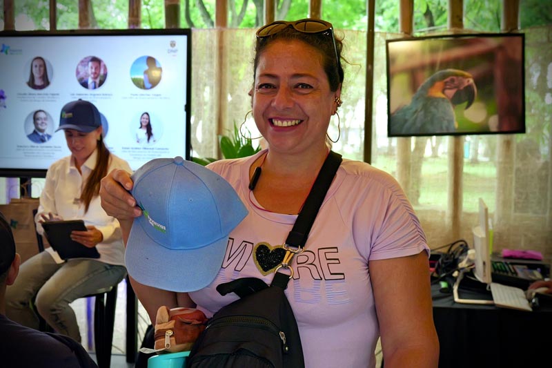 Mujer de mediana edad, sonríe feliz al recibir una gorra azul de premio por su participación.  