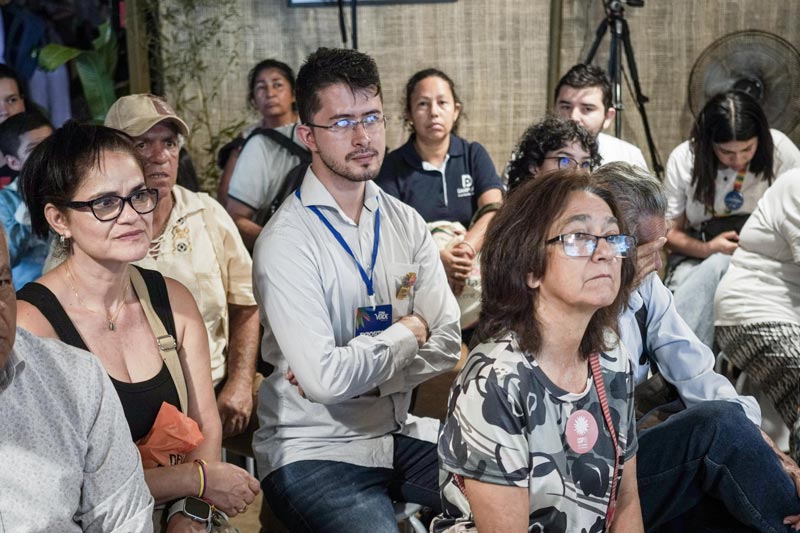 Estand lleno de personas de todas las edades, varios tomando apuntes y concentrados en la charla. 