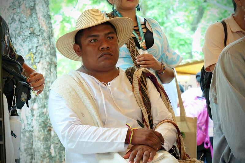 Hombre joven de comunidad indígena, viste traje típico de la comunidad Wayuu. Está concentrado en la charla. 