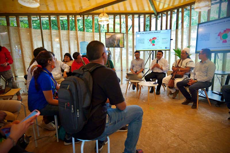 Estand lleno de personas que escuchan atentamente las intervenciones de los panelistas.