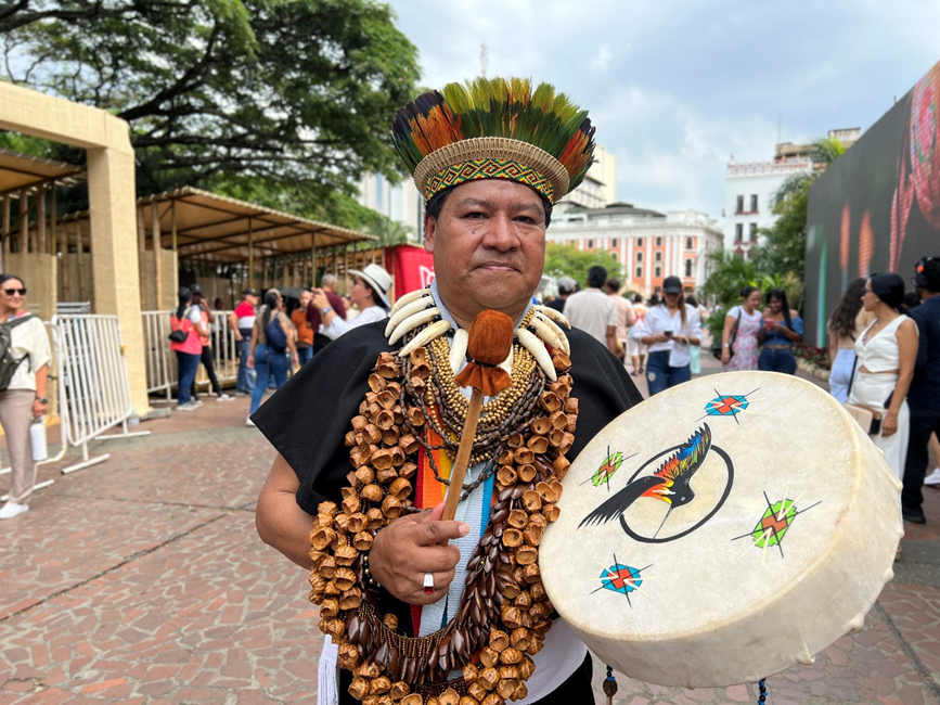 Indígena toca el tambor bordado con un ave ancestral, mientras camina entre la gente de la COP16.